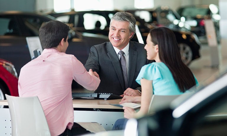 Couple shaking hands with car salesman